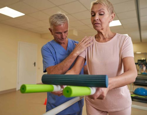 Stroke patient does exercises for coordination improving while healthcare worker next to her helping during rehabilitation in medical center
